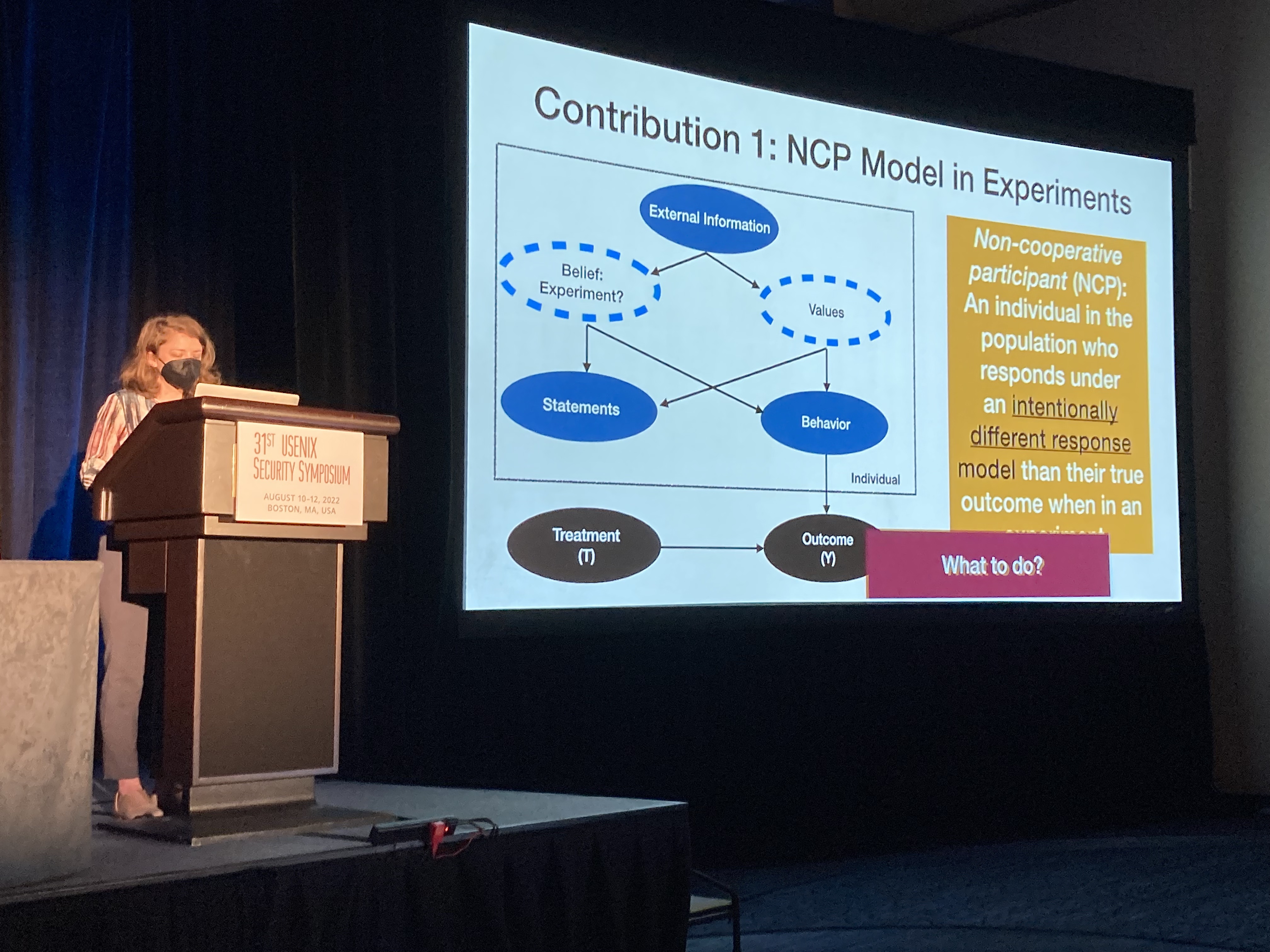 Kaleigh Clary presenting her work. Slide depicts the scenario as a causal model, where non-cooperative behavior is defined as the case where participants behave differently when they believe they are being surveilled.